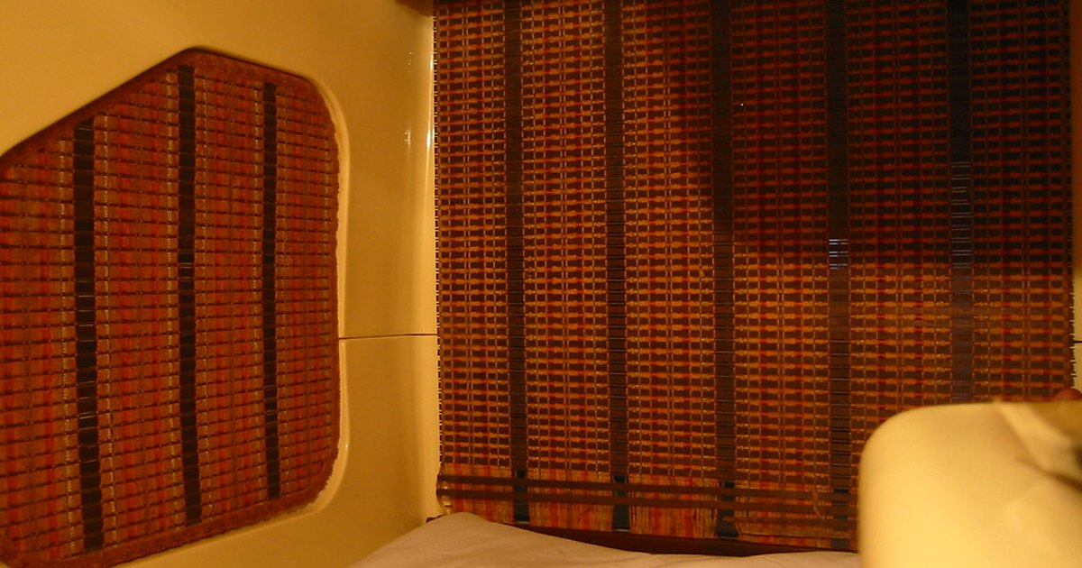 Interior of a capsule hotel pod with white bedding and woven blinds over the entrance
