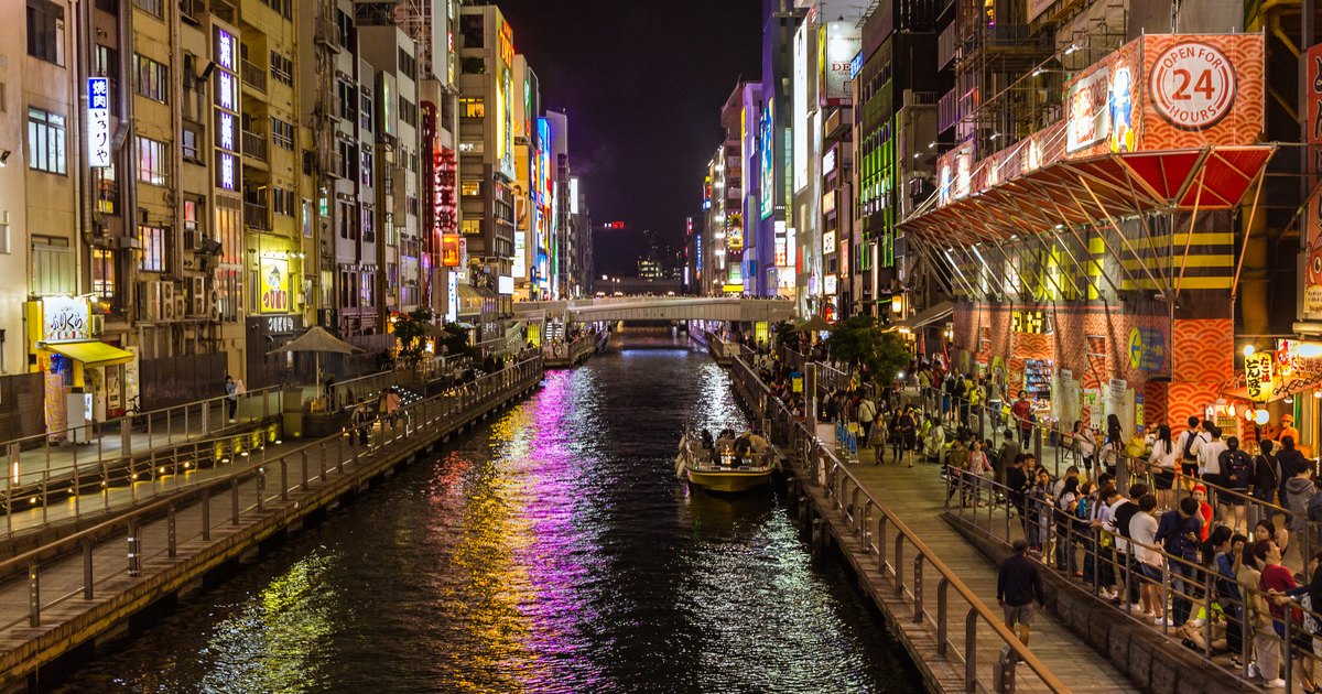 Dotonbori canal at night with a boat on the water, lit signs and crowds along both banks