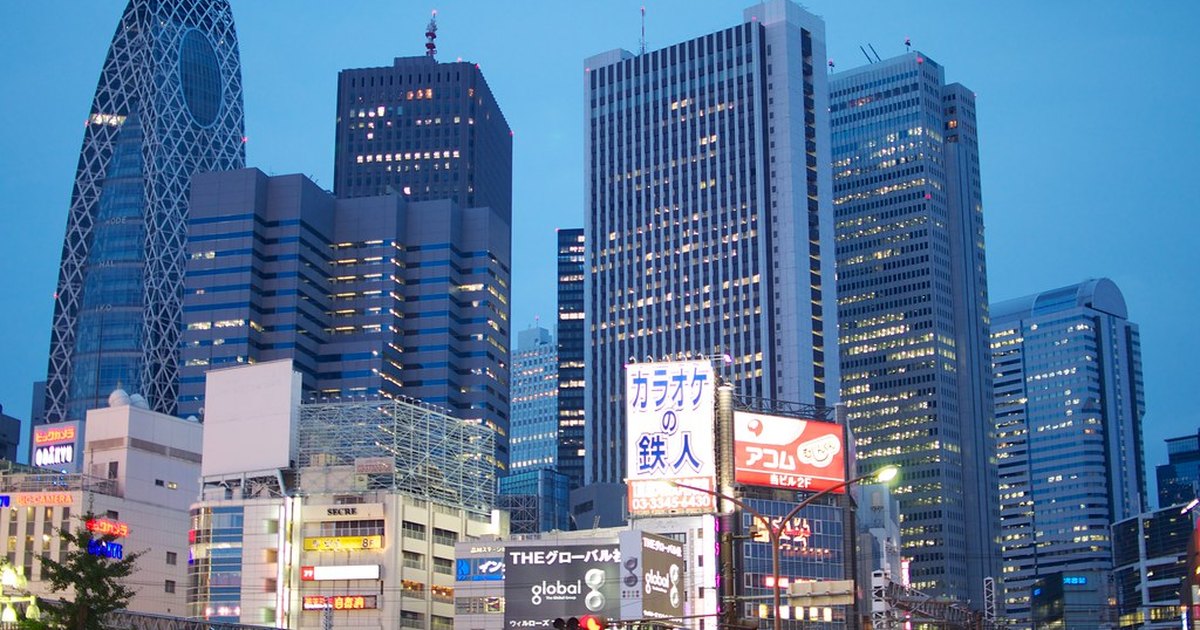 Nishi-Shinjuku skyscraper cluster at dusk with a train passing in the foreground