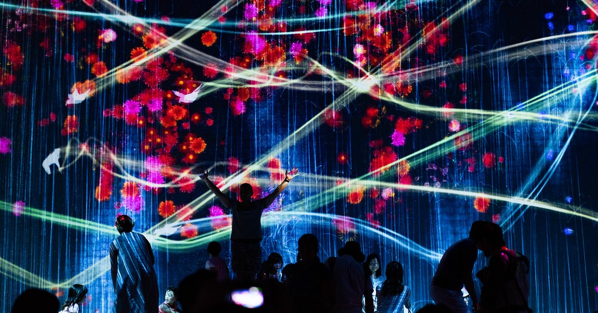 Visitors silhouetted in a darkened room filled with projected digital art