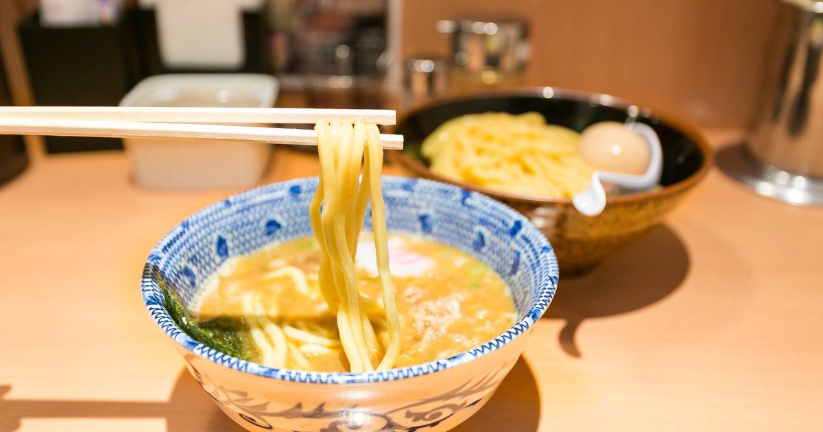 Chopsticks lifting tsukemen noodles over a bowl of dipping broth at a restaurant counter