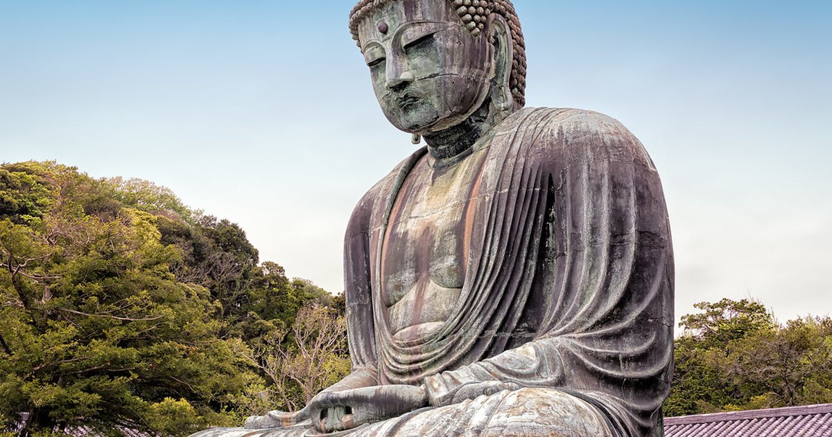 The Great Buddha of Kamakura seated in the open air with wooded hills behind