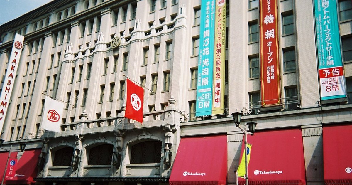The stone facade of the Nihonbashi Takashimaya department store with red awnings and hanging banners