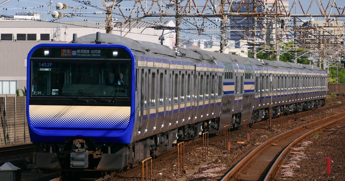 A blue-and-cream JR Yokosuka Line train curving along the tracks toward the camera