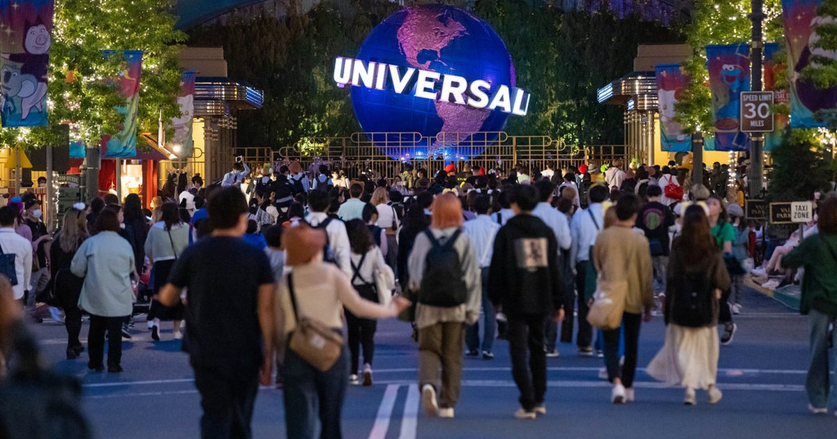 The illuminated Universal globe at the park entrance with visitors walking toward it in the evening