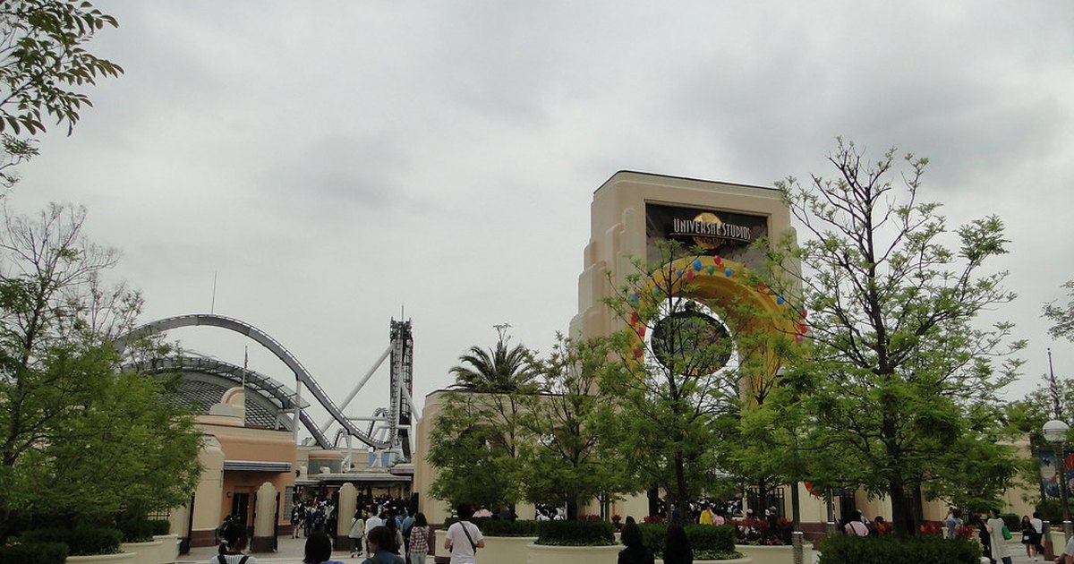 A walkway inside Universal Studios Japan with landscaped planters and a roller coaster arcing in the distance