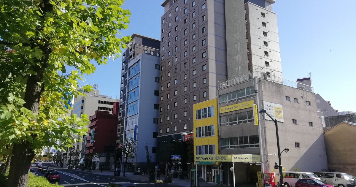 APA Hotel tower in Hiroshima rising above a wide boulevard, rooftop signage visible as part of the city streetscape