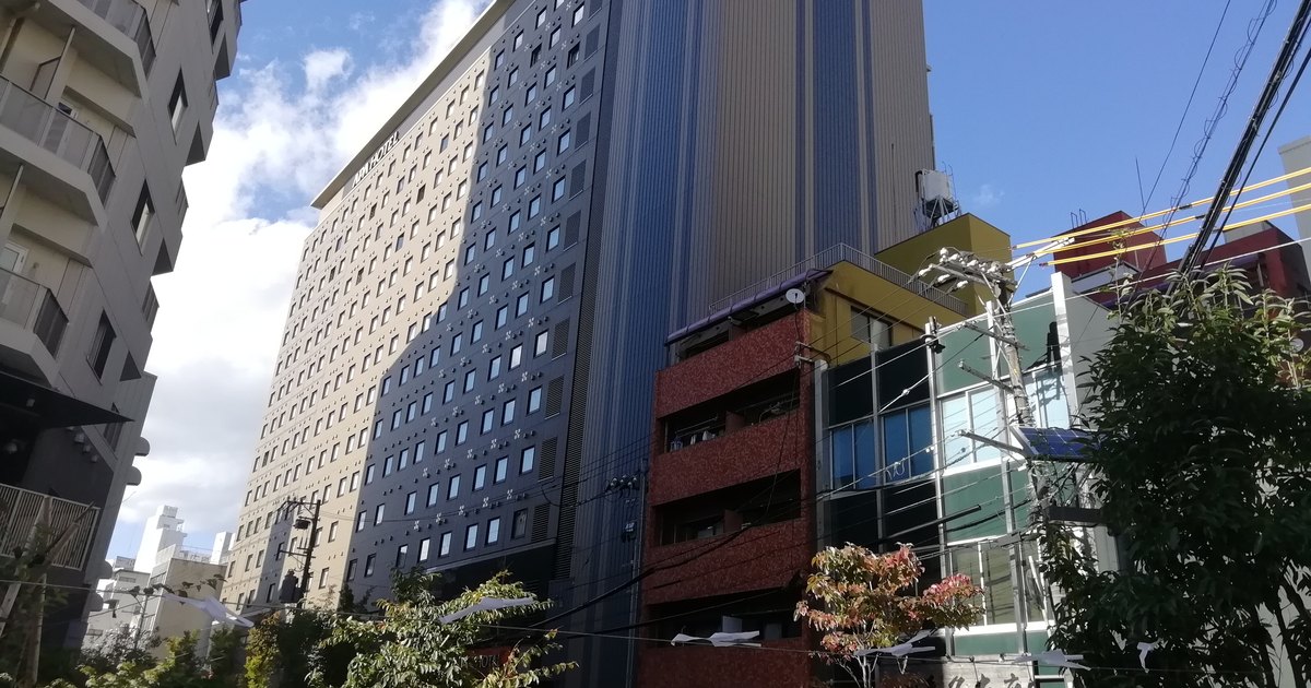 Upward view of an APA Hotel high-rise facade with rows of identical windows against a blue sky
