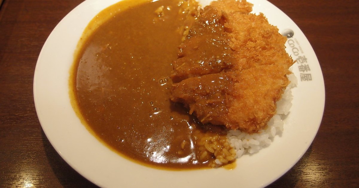 Katsu curry on a white plate with dark curry sauce pooling beside the rice, photographed at a CoCo Ichibanya counter