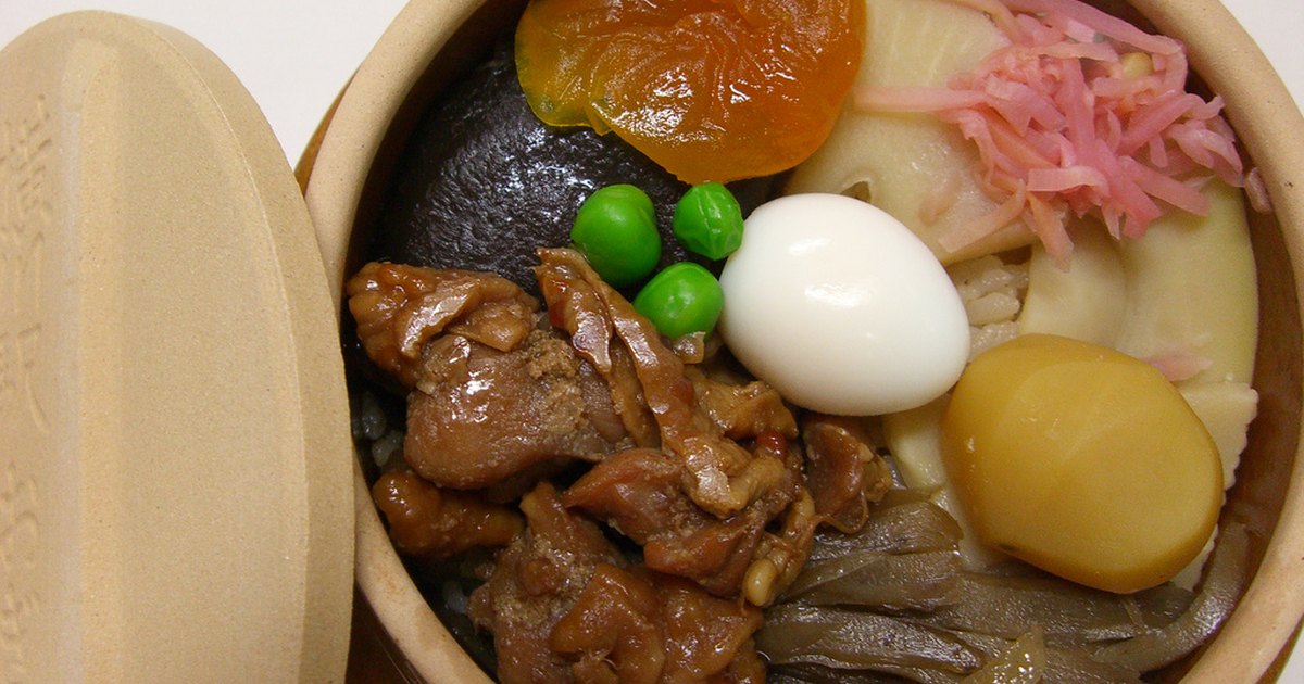 Toge no Kamameshi ekiben opened to show chicken, quail egg, chestnut and vegetables over rice inside its ceramic pot, lid resting beside it