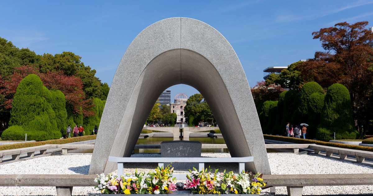 Memorial Cenotaph in Hiroshima Peace Memorial Park with flowers laid before it and the Atomic Bomb Dome framed through its arch
