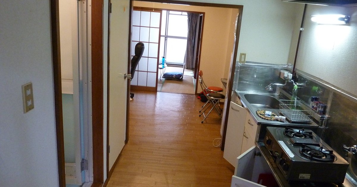 Compact Japanese apartment kitchen with gas stove and sink, looking through to a tatami living room