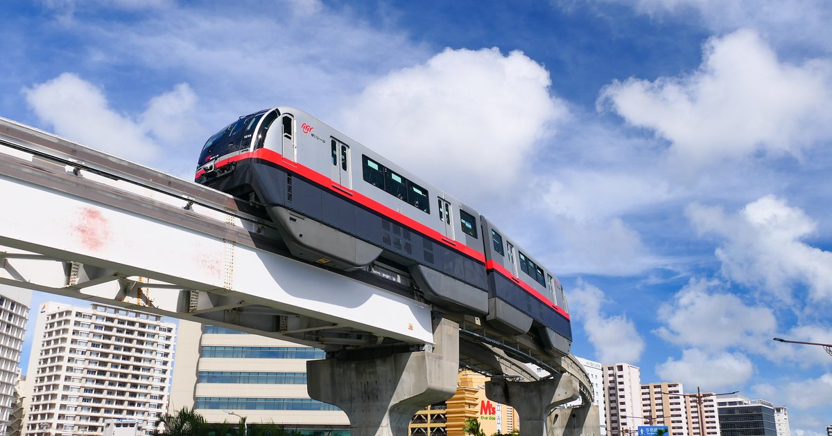 Yui Rail monorail train running on its elevated track above central Naha under a bright blue sky