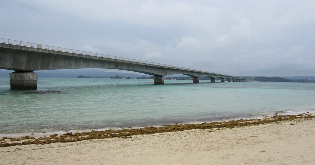 Kouri Bridge stretching across shallow turquoise water toward Kouri Island, seen from the beach