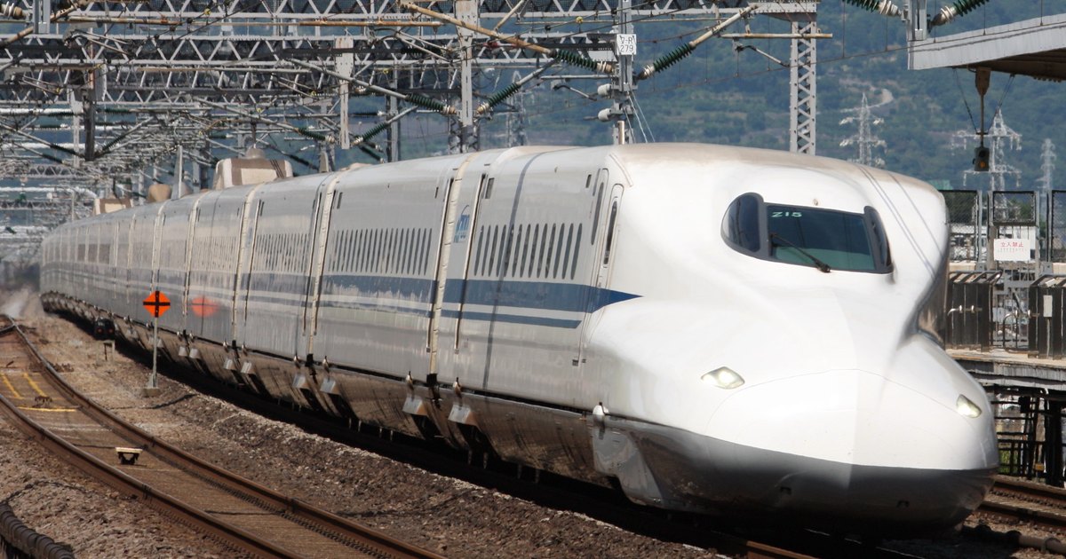 N700 series Tokaido Shinkansen train rounding a curve at speed, white body with blue stripe under overhead catenary