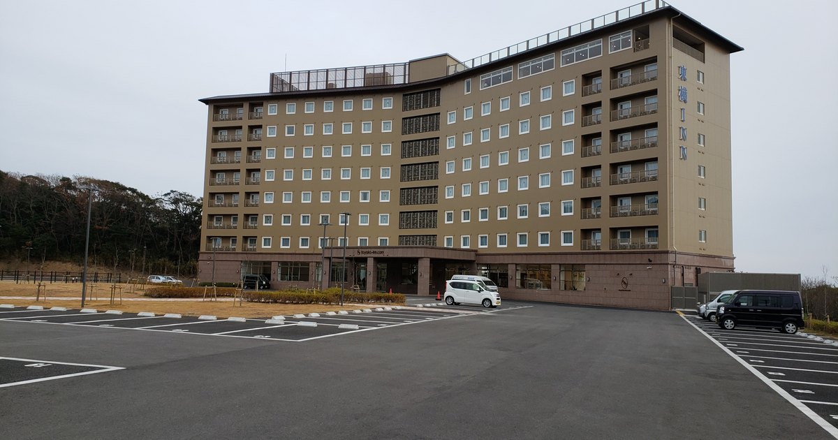 Toyoko Inn in Tsushima Hitakatsu, a low-rise beige hotel building with parking lot in front, on an overcast day