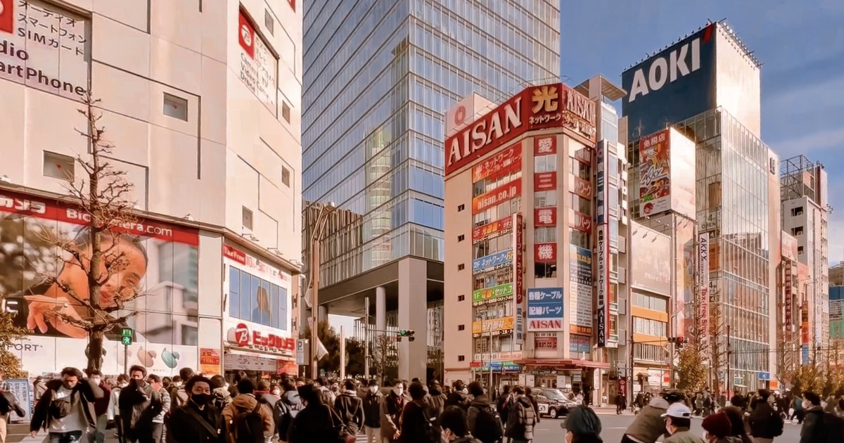 A crowd of pedestrians crossing a wide street in Akihabara with electronics stores behind