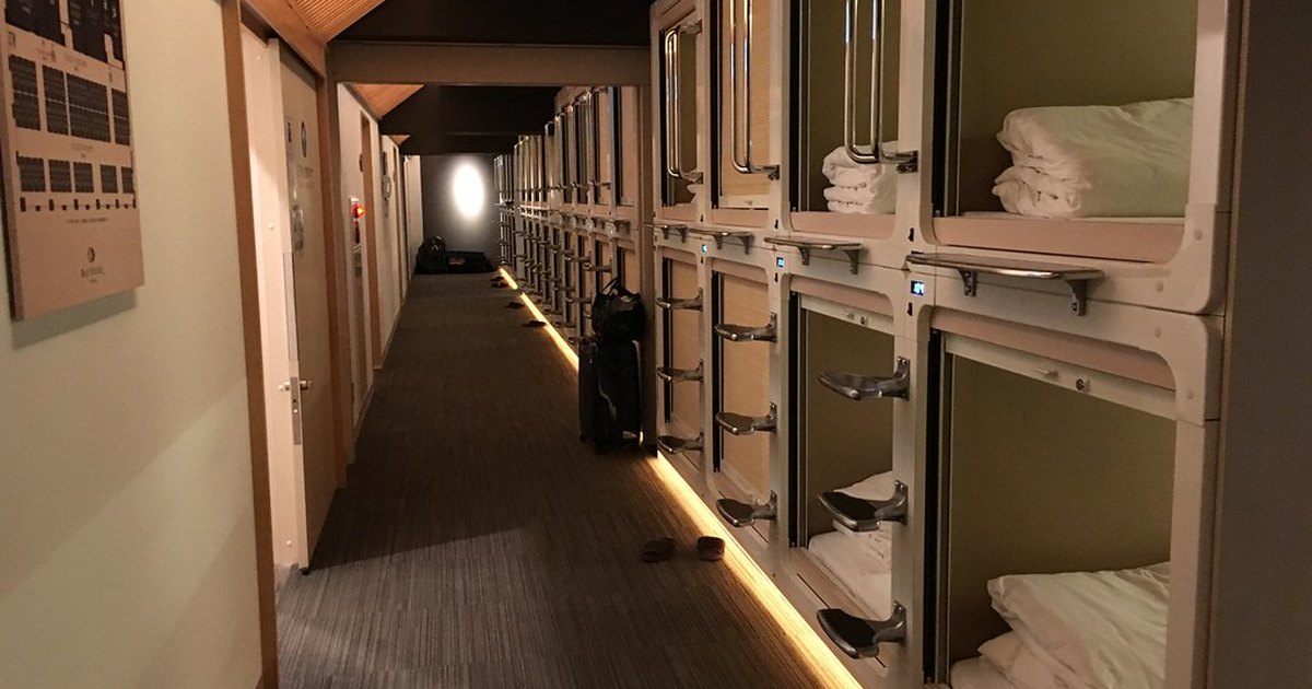 Dim corridor of stacked sleeping capsules with folded towels and bedding at a Tokyo capsule hotel