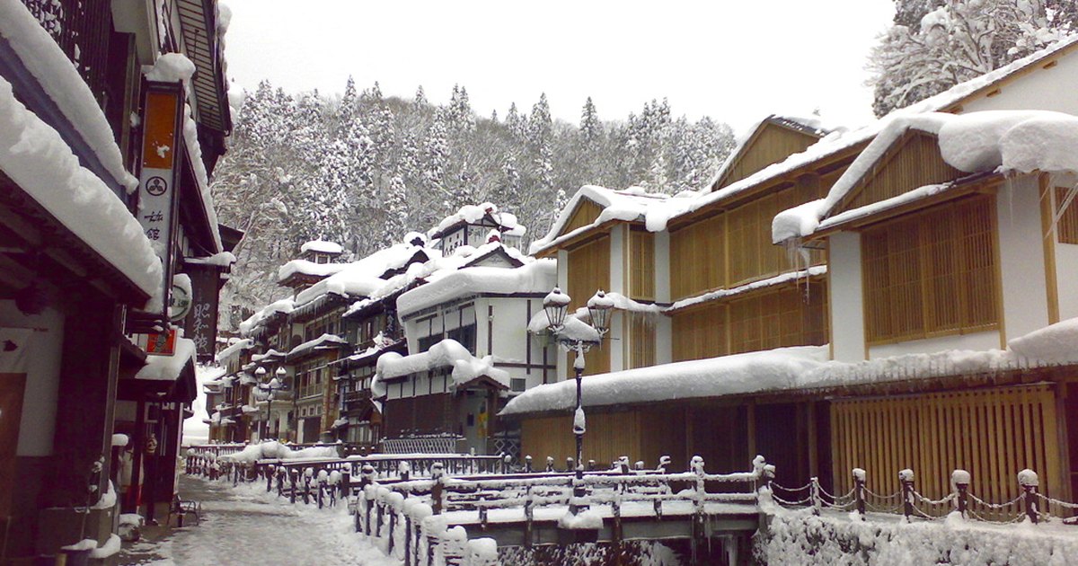 Snow-covered multi-story wooden ryokan buildings lining the canal at Ginzan Onsen