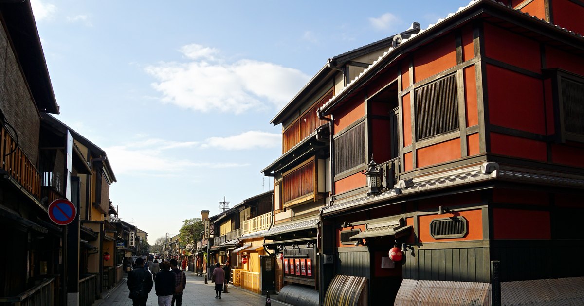 Hanamikoji Street in Gion, Kyoto, lined with traditional wooden machiya townhouses, with the red-walled Ichiriki teahouse on the corner