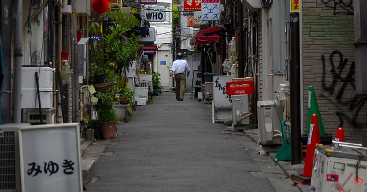 Narrow daytime lane in Shinjuku Golden Gai lined with small closed bars and hanging signs