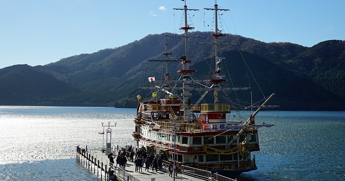 A sightseeing ship styled as a galleon tied up at a pier on Lake Ashi, with the caldera rim rising behind it