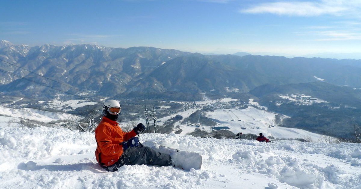 Snowboarder resting on a ridge above the Hakuba valley with ski runs and mountains below