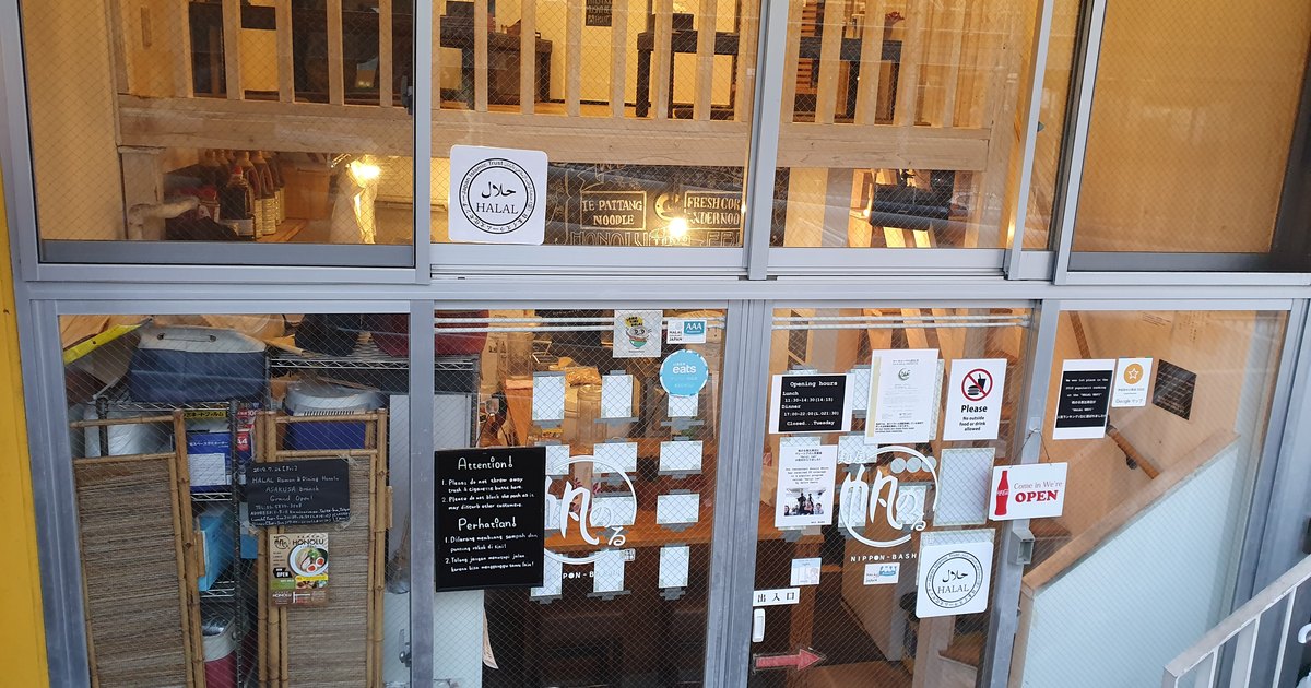 Storefront of a halal ramen restaurant in Ebisu, Tokyo, with halal certification stickers, opening hours, and multilingual notices on the glass door