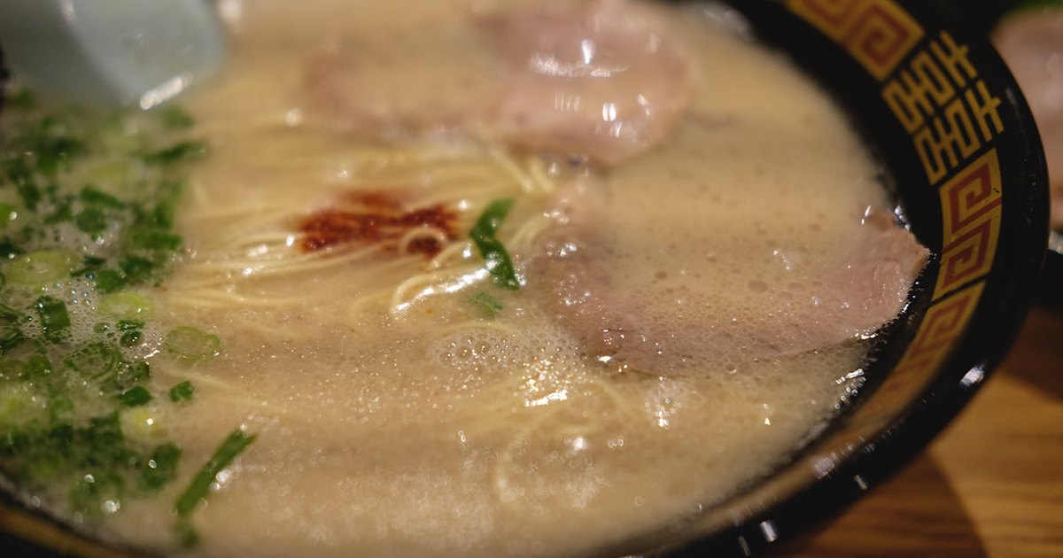 Close-up of an Ichiran tonkotsu ramen bowl with milky pork broth, thin noodles, chashu slices, green onion and a dab of red spicy sauce