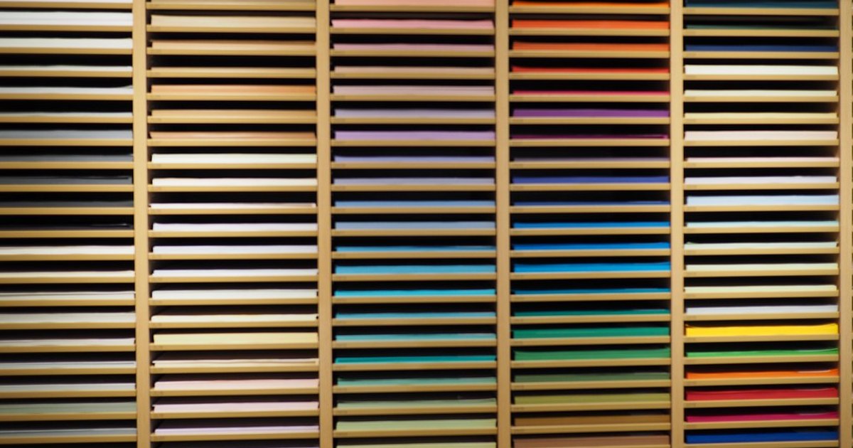 Wall of wooden racks holding hundreds of sheets of paper arranged by color in a Ginza stationery store