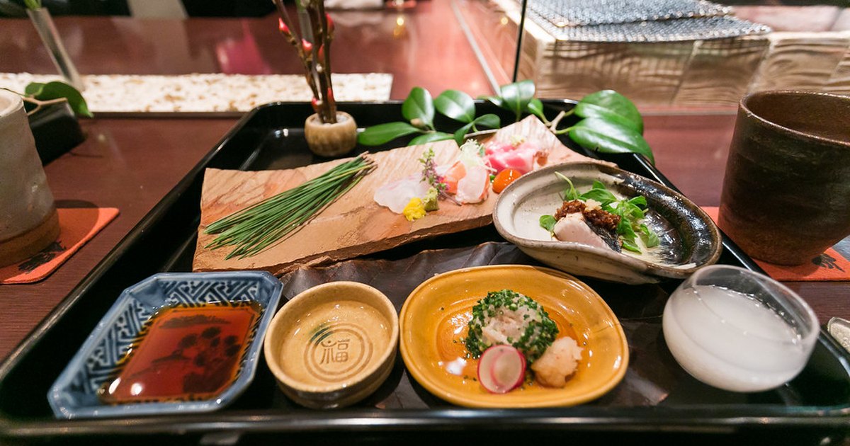 An artfully arranged appetizer tray with sashimi, small ceramic dishes and sake at a Japanese restaurant counter