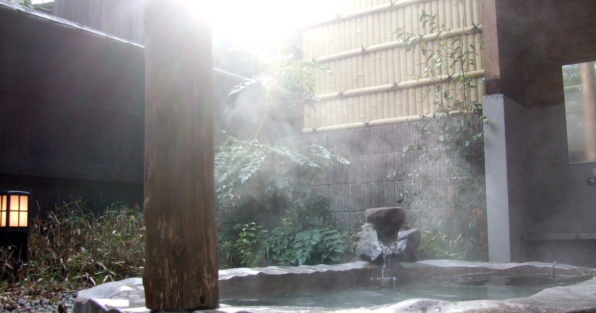 Steam rising from an outdoor stone onsen bath enclosed by a bamboo screen in Japan