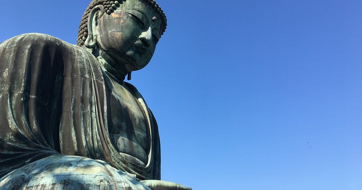 Low-angle view of the bronze Great Buddha of Kamakura against a clear blue sky