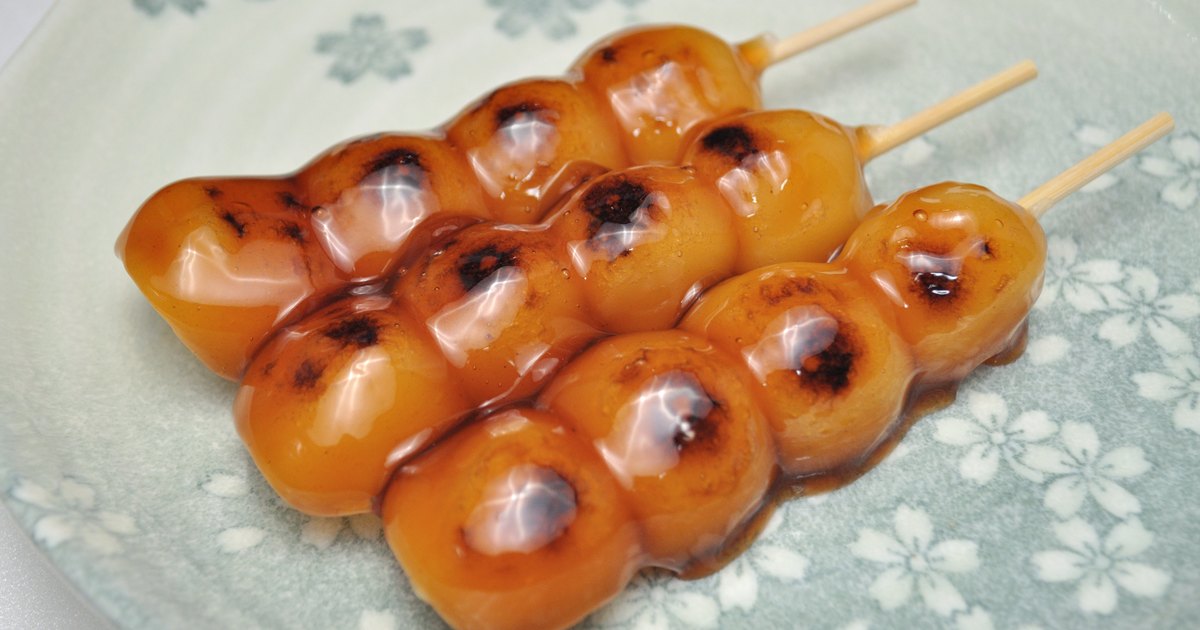 Three skewers of glossy soy-glazed mitarashi dango on a cherry-blossom patterned plate