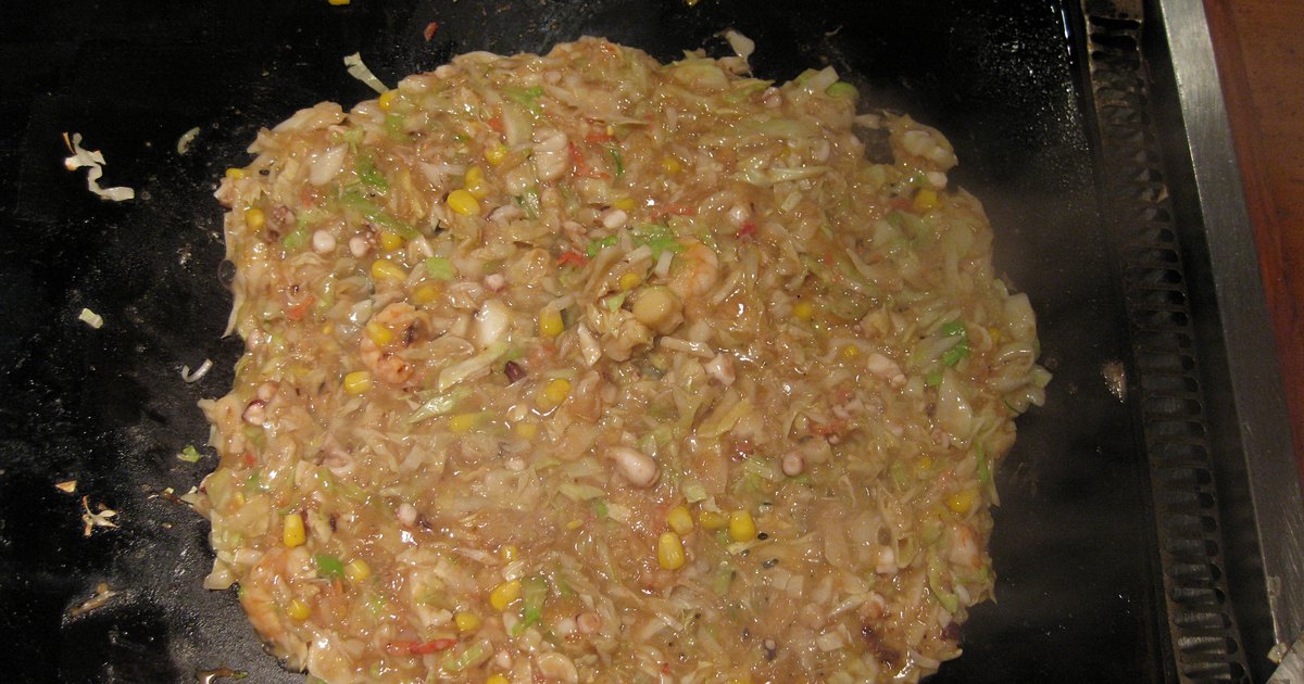Runny monjayaki batter with cabbage, corn and seafood spreading across a black tabletop teppan griddle