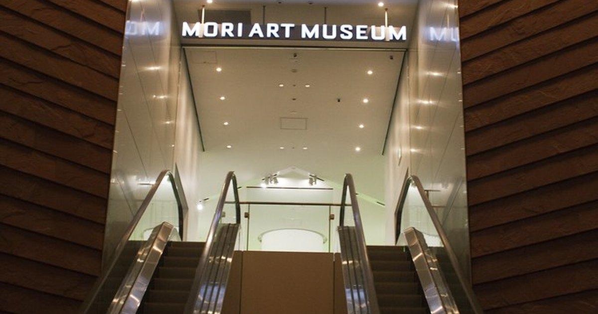 Escalators rising toward the illuminated Mori Art Museum sign inside Roppongi Hills
