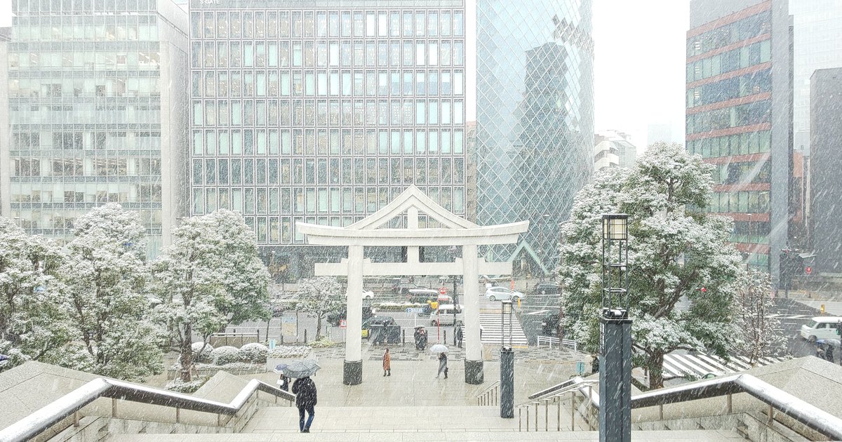 A stone torii gate at Hie Shrine in Nagatacho during heavy snowfall with office towers behind