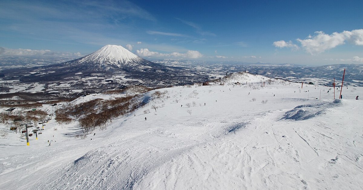 Skiers on a wide snowy slope at Niseko Annupuri with the cone of Mount Yotei across the valley