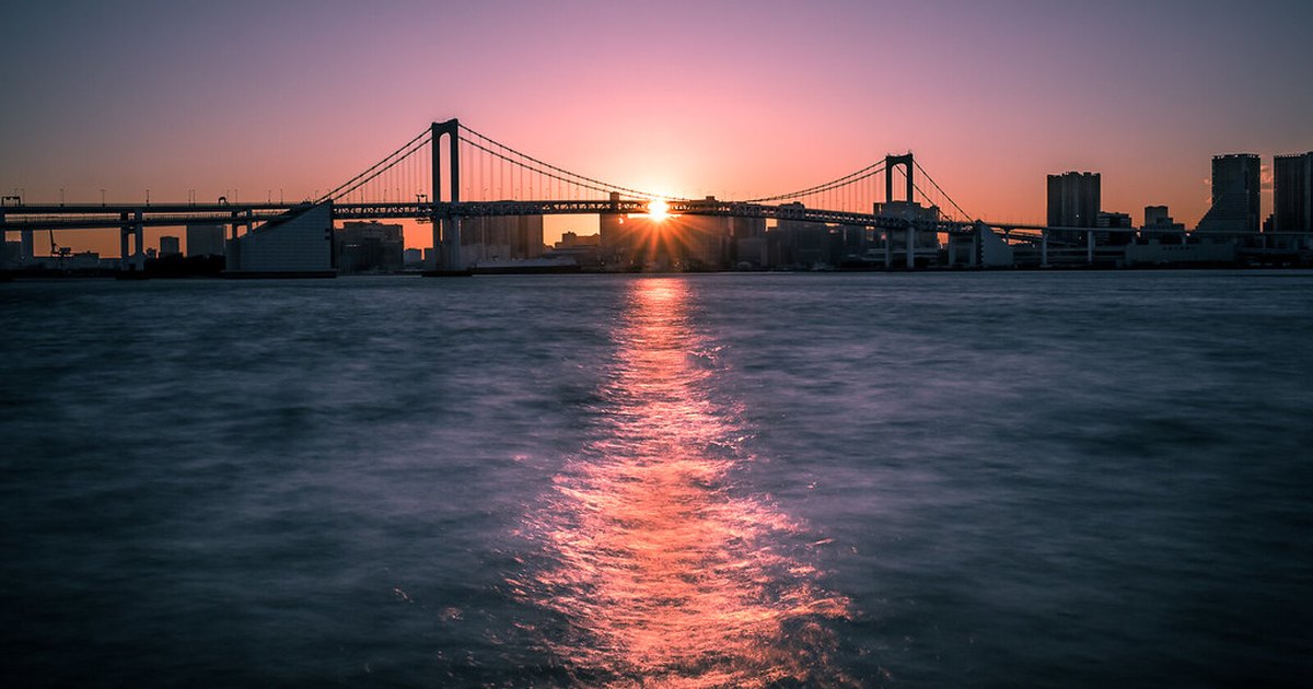 Rainbow Bridge silhouetted against a pink sunset over Tokyo Bay