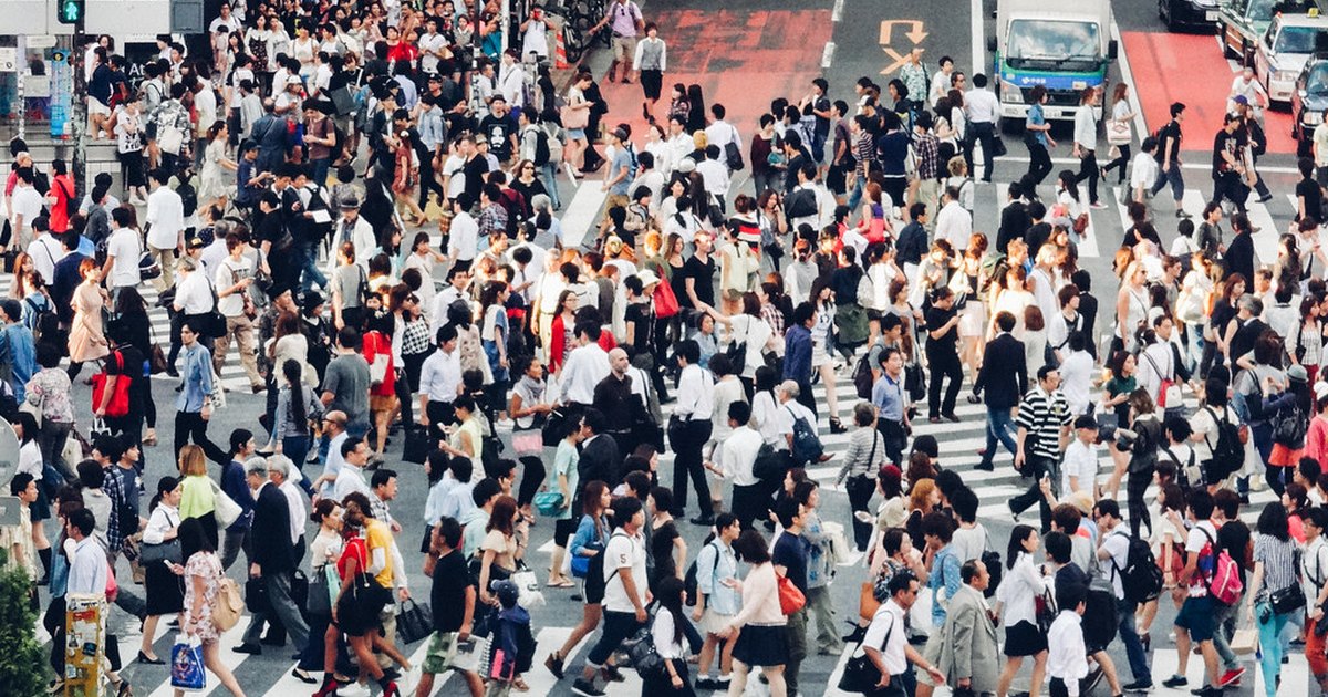 Crowds of pedestrians walking across the striped crosswalks of Shibuya Crossing seen from above