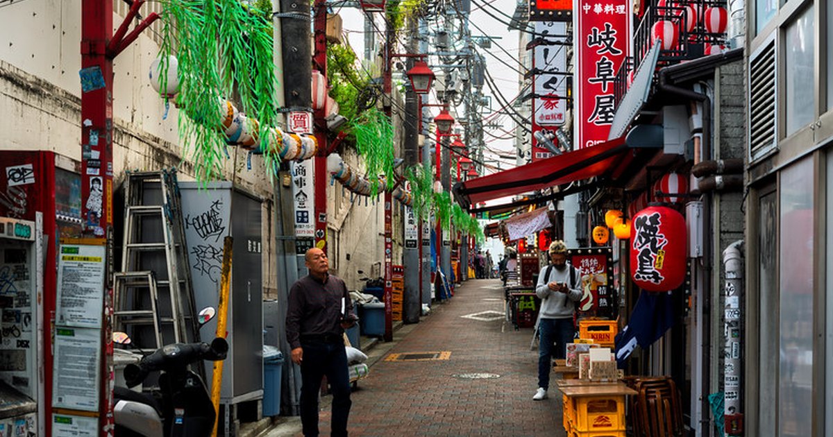 A narrow paved alley lined with small izakaya, vertical signboards and red lanterns in Shinjuku