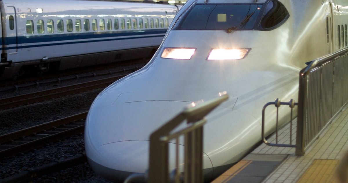 Close view of the nose of a white shinkansen train with its headlights lit at a platform