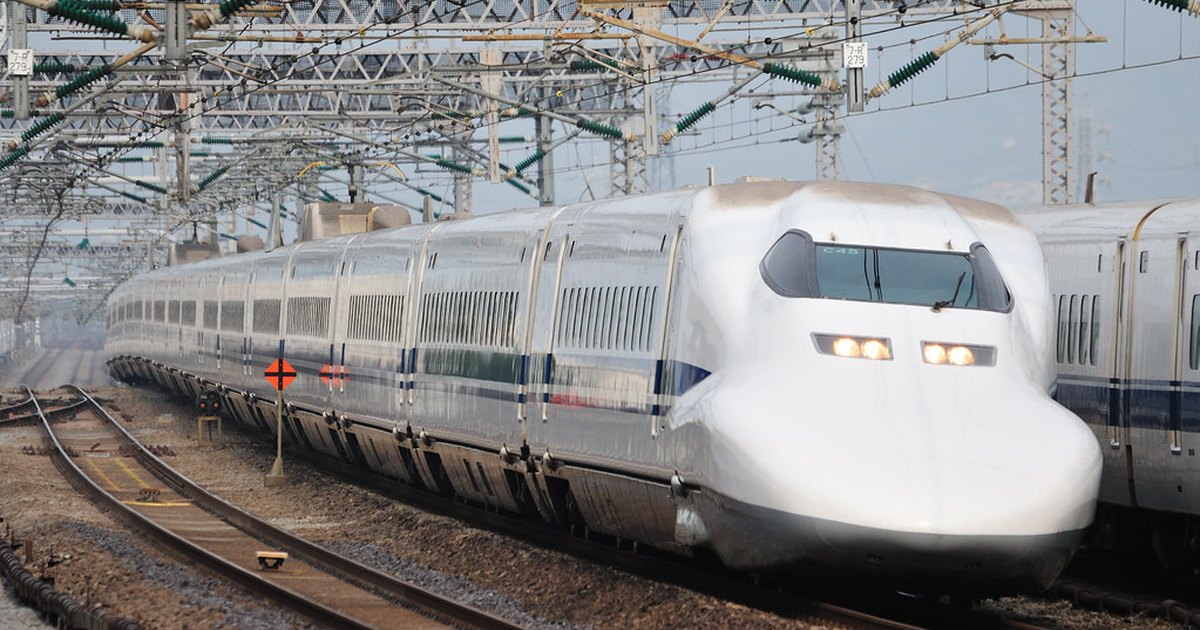 A white Shinkansen train with a long pointed nose running past overhead power lines