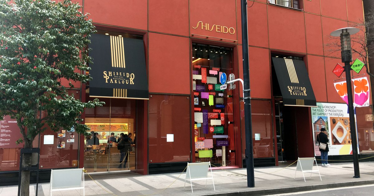 Red facade of the Shiseido Parlour building in Ginza with black-and-gold awnings over the street-level shop entrances