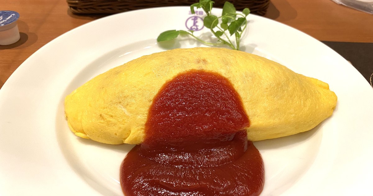 Classic omurice at Taimeiken with a smooth pale-yellow omelette over rice and a pool of ketchup on a crested plate