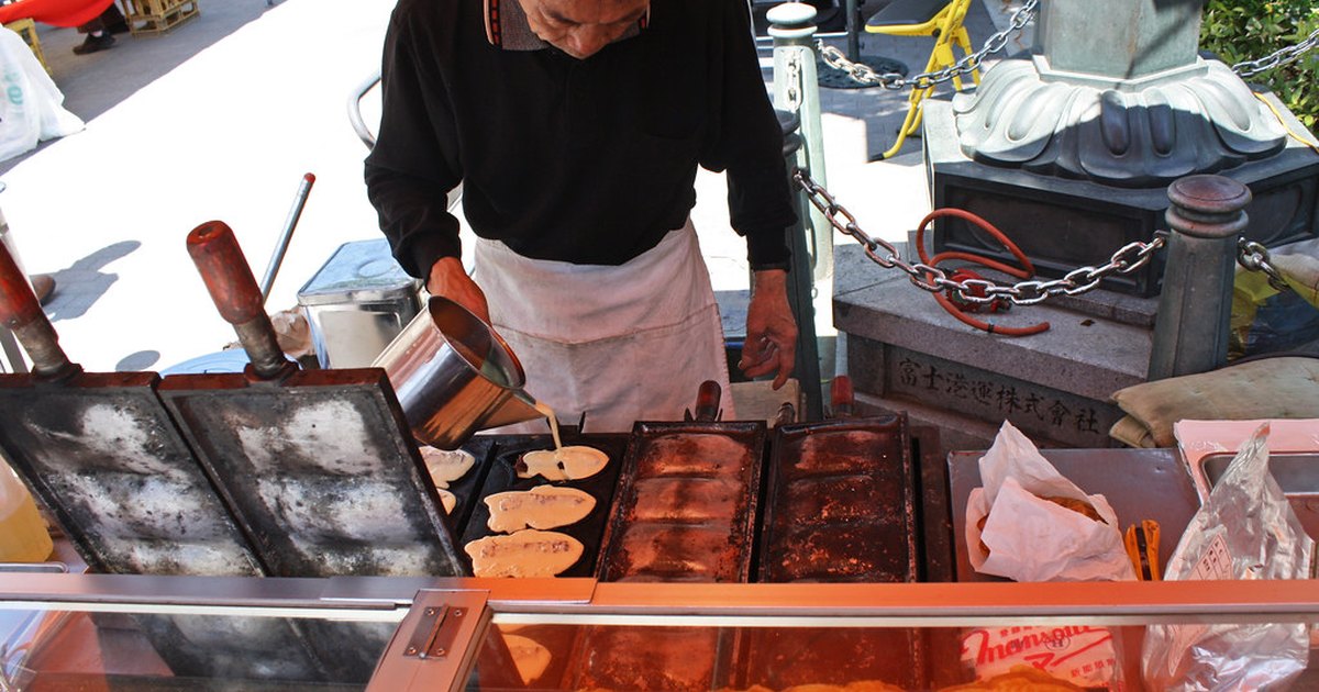 A vendor pouring batter into fish-shaped iron molds at an outdoor taiyaki stall