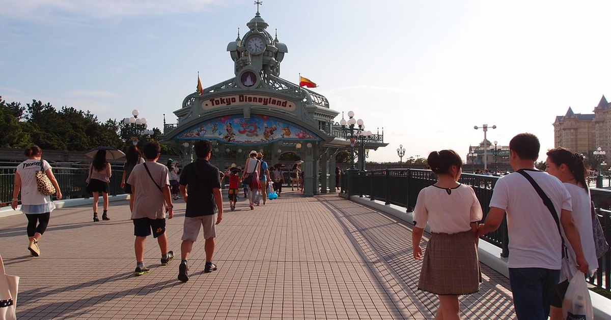 Visitors walking along the promenade toward the Tokyo Disneyland entrance gate on a sunny day