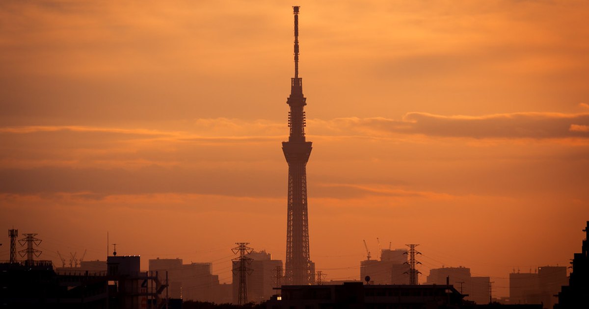 Tokyo Skytree silhouetted against an orange sunset sky above a low skyline