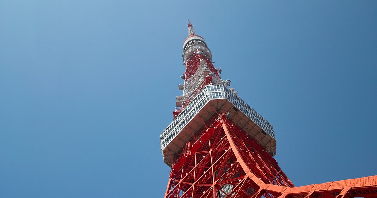Tokyo Tower photographed from directly below, its red and white lattice steelwork against a blue sky