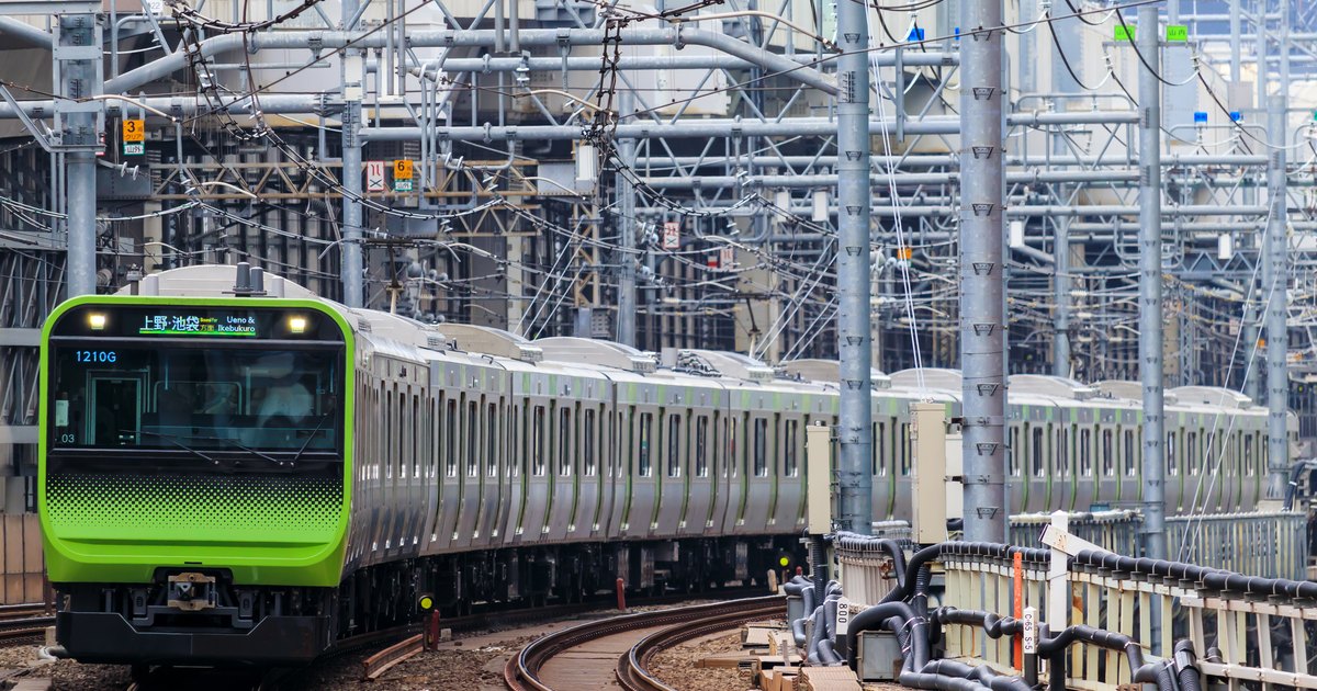 A green-striped Yamanote line commuter train rounding a curve in central Tokyo